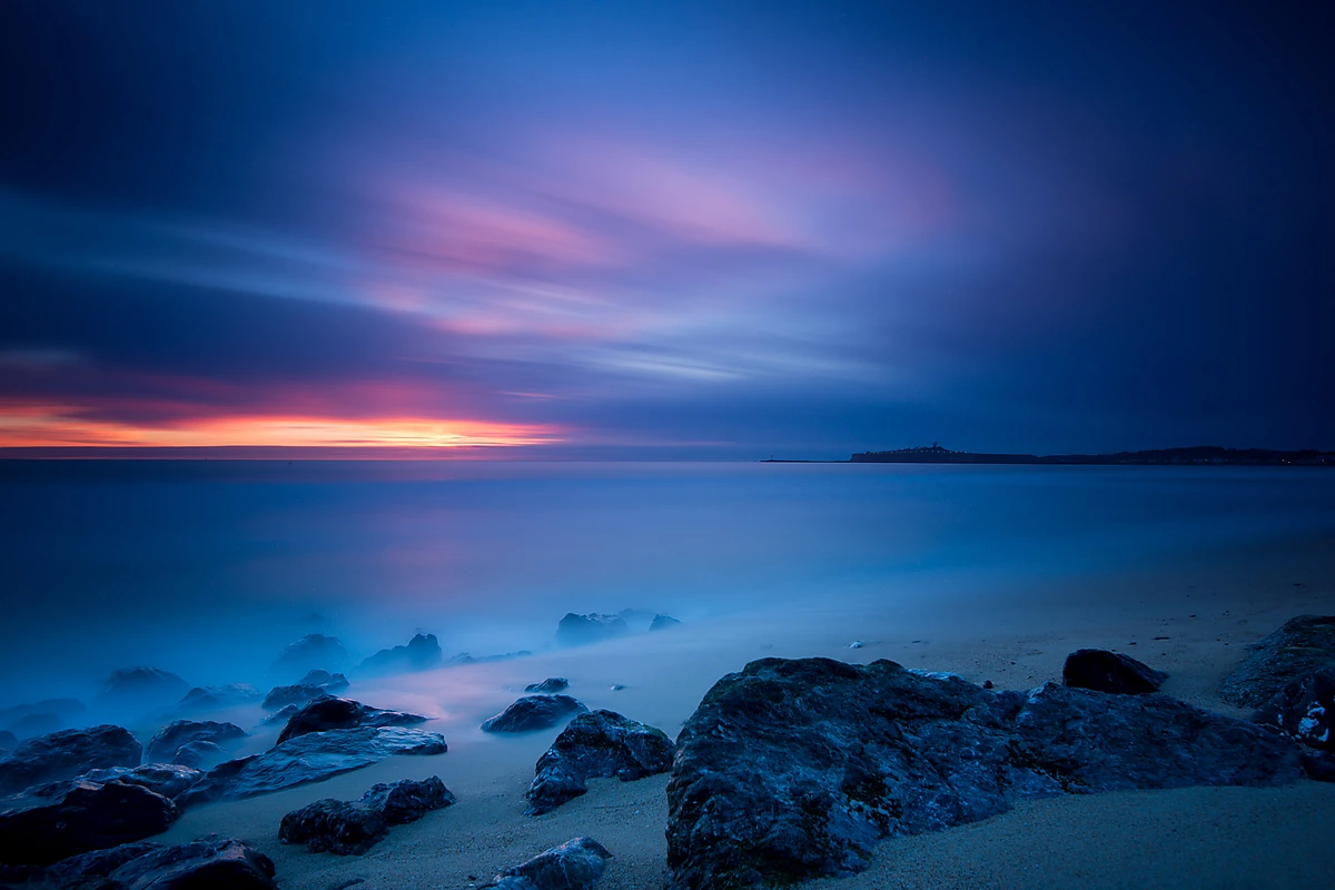 The sun breaks through the clouds as it sets over the coast.