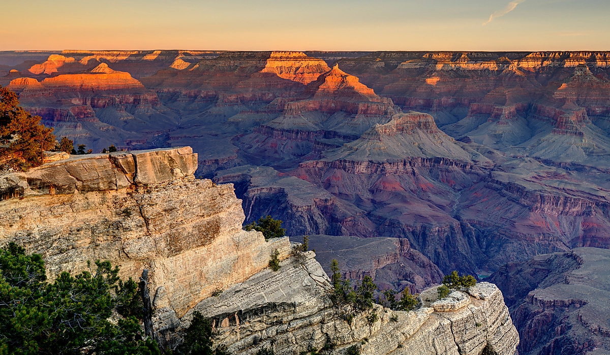 Sunrise illuminates the upper cliffs of the Grand Canyon in warm orange light above layers of shadowed canyon walls at Mather Point.