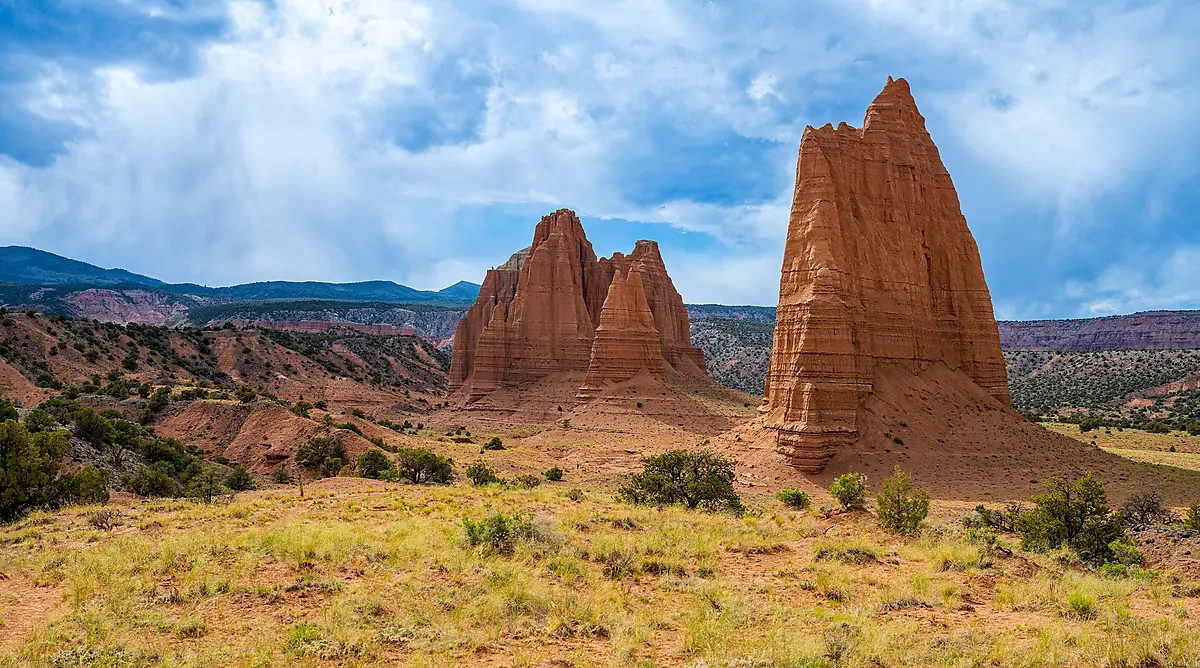 Towering red sandstone monoliths rise above grasses and desert vegetation beneath dramatic clouds in Upper Cathedral Valley, Capitol Reef National Park.